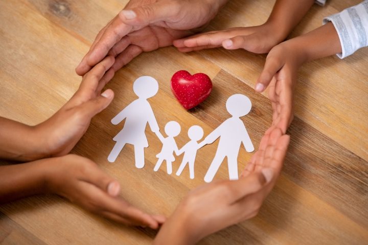 Family law showing a circle of hands, around a paper cut out of a family and heart.